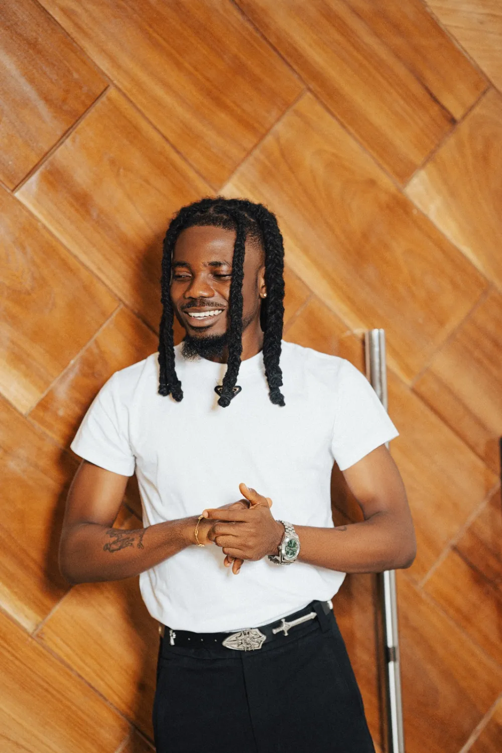 Emmy Blaq smiling in a white T-shirt against a wooden wall